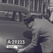 Kenteken: A 29223; G. W. J. Meijer opent de kofferbak van zijn Kaiser Frazer, foto: still uit de film "Reis personeel tentoonstelling", Groothuis, 1953, coll. GrA (2209-4524)