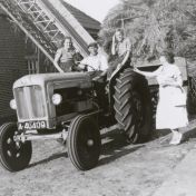Kenteken: A 40409; Jullo Flink en twee kinderen op de Fordson Major tractor, met aanhangwagen vol korenschoven, daarnaast zijn vrouw Iektje Flink-van Hateren, Hebrecht, ca. 1951 (2437-5505)