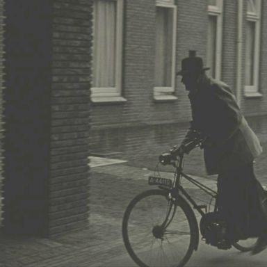 Kenteken: A 44119; Dokter van Eck stapt van zijn fiets met hulpmotor bij het Academisch Ziekenhuis in Groningen, foto: still uit de film "Een dag in de chirurgische kliniek", Foto-kino Wedema & Dijk, Bosman (regie), 1950 coll. GrA (2209-AV0472)